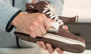 Mani che puliscono una scarpa di pelle scamosciata marrone con una spazzola, mostrando come pulire le scarpe di pelle.