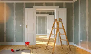 Rullo, secchio di vernice rossa e scala in legno pronti per togliere macchie di vernice secca dalle pareti di una stanza in ristrutturazione.