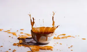 Un caffè schizza da una tazza, creando un'onda liquida. Le macchie di caffè vanno via, lasciando una scia dorata sulla superficie bianca.