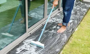 Persona a piedi nudi lava il marmo esterno annerito con una scopa e schiuma.
