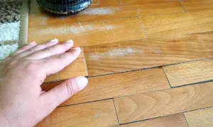 Mano su parquet graffiato, pronto per essere pulito con aceto e bicarbonato per un restauro fai-da-te.