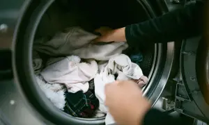 Mani che caricano la lavatrice con vestiti chiari. Speriamo che l'ammorbidente non lasci macchie sui vestiti.
