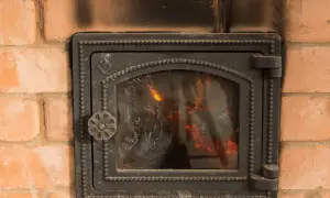Porta del camino in ghisa annerita dal fumo, con fiamme visibili all'interno. Utile per capire come pulire il marmo del camino annerito.