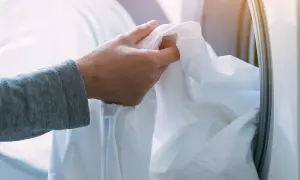 Mano che inserisce un lenzuolo bianco nella lavatrice. Ricorda che candeggina e bicarbonato si possono mischiare con cautela per un bucato più bianco.