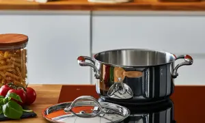 Pentola in acciaio lucido, coperchio e ingredienti freschi sul piano cottura. Scopri come pulire le pentole in acciaio per mantenerle splendenti.