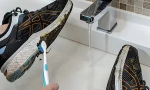 Come lavare le scarpe da running: una mano con uno spazzolino pulisce il fango dalla suola di una scarpa sotto un rubinetto aperto.