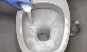 Guanto blu versa polvere bianca nel WC per disincrostare. Bottiglia d'acqua sullo sfondo.
