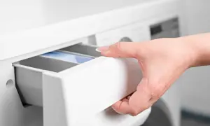 Mano inserisce cassetto lavatrice con percarbonato e candeggina.