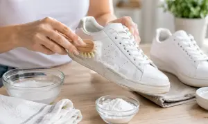 Mani che puliscono scarpe bianche con una spazzola, mostrando come lavare le scarpe con bicarbonato e sapone.