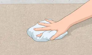 Mano che tampona una macchia su tessuto beige con un panno bianco. Guida su come togliere macchia d'olio.