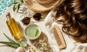 Olio, aloe e pettine in legno per curare i capelli secchi. Cappello di paglia e occhiali da sole completano la scena estiva.