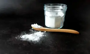 Un cucchiaio di legno con bicarbonato, pronto per smacchiare con bicarbonato. Un barattolo di vetro pieno di polvere bianca sullo sfondo.