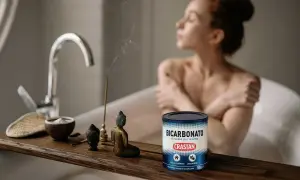 Una donna rilassata in vasca da bagno, con incenso e una ciotola di bicarbonato di sodio purissimo, un prodotto versatile per la casa e l'alimentazione.