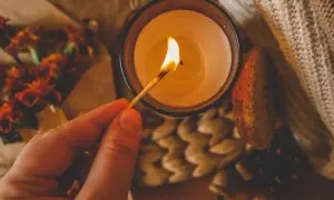Un fiammifero illumina una candela, un modo per spegnere le candele senza fare fumo. Atmosfera autunnale con fiori e zucca.