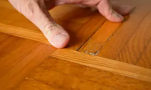 Dito come togliere la cera dal parquet verniciato: un dito indica una crepa sul legno lucido, mostrando il problema.
