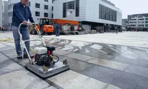 Uomo pulisce autobloccanti con idropulitrice in una piazza. L'acqua riflette la luce sui blocchi di pietra.