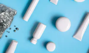 Pietra grezza e piccoli frammenti metallici accanto a flaconi e tubetti bianchi, evocano la purezza dei cosmetici nichel free.