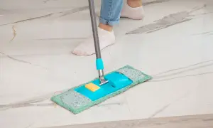Piedi in calzini bianchi puliscono un pavimento in marmo con uno straccio blu e verde. Ecco come pulire il marmo per farlo brillare.