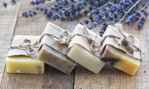 Saponi ecologici artigianali, avvolti in carta e legati con spago, su un tavolo di legno con fiori di lavanda.