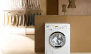 Lavatrice Miele bianca con ingresso acqua calda e fredda, accanto a un armadio con abiti ordinati.