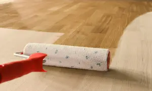 Rullo per verniciatura parquet in azione, che stende una mano di vernice su un pavimento in legno chiaro, creando un effetto bagnato e lucido.