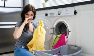 Donna con espressione disgustata annusa un panno giallo, i panni in lavatrice puzzano.