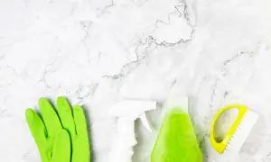 Guanti verdi, spray bianco, flacone di liquido verde e spazzola gialla pronti per scoprire come pulire pietra.