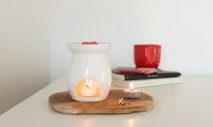 Diffusore bianco con candela accesa e cubetti di cera profumata sopra. Un'altra candela e fiammiferi completano la scena, mostrando che cos'è la cera per profumare l'ambiente.