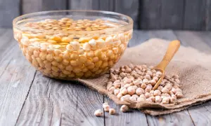 Ceci sono ceci in ammollo tutta la notte in una ciotola di vetro. Accanto, ceci secchi su tela grezza con un cucchiaio di legno.