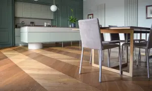 Un elegante parquet a spina di pesce in legno crea un motivo a zig-zag, che si estende dalla cucina moderna alla zona pranzo.