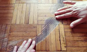 Mani sul parquet rovinato, graffi e segni evidenti. Si cerca una soluzione per pulire e ripristinare il legno.