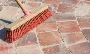 Una scopa con setole rosse su sanpietrini rossi e sabbia. Un modo semplice per capire come pulire i sanpietrini.