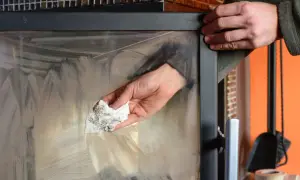 Mani che puliscono il vetro della stufa a legna con un panno sporco di fuliggine, mostrando come pulire il vetro della stufa a legna.