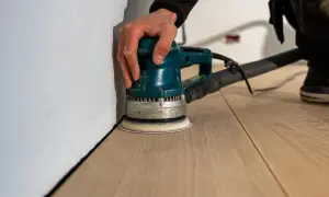 Mano che usa una levigatrice per levigare parquet a mano, creando una superficie liscia e pronta per la finitura.