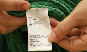 Etichetta di un maglione verde: non usare candeggina su poliestere. Asciugare in piano, usare un detergente delicato.