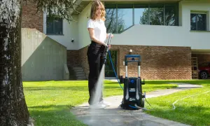 Donna usa idropulitrice per pulire il sentiero di cemento, mostrando come togliere il muschio.