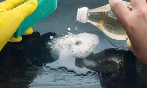 Mano con guanto giallo pulisce con spugna. Aceto sgrassa la superficie, creando schiuma.