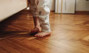 Bambino con pigiama a mongolfiere sui piedi nudi su un parquet lucido, pronto per scoprire come pulire il parquet dopo i lavori.
