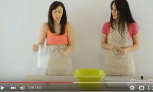 Due donne con grembiuli a pois mostrano come sbiancare asciugamani con candeggina, versando liquidi in un contenitore giallo.