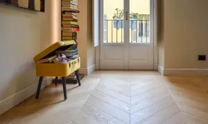 Un elegante parquet a spina di pesce, con finitura opaca, riflette la luce che entra dalla porta-finestra.