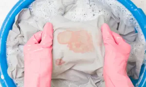 Mani con guanti rosa che lavano un vestito macchiato di rosso in una bacinella blu con acqua saponata. Ecco come sbiancare i vestiti che hanno preso colore.