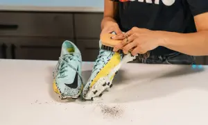Mani che spazzolano scarpe da calcio sporche di fango, un passo fondamentale per capire come lavare le scarpe da calcio e mantenerle in forma.