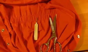 Tuta da meccanico arancione, forbici e un infila ago. Pronti per lavare le tute da meccanico in lavatrice.