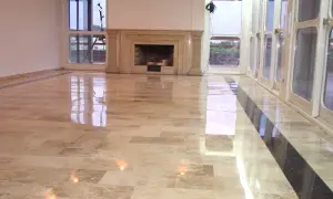 Pavimento in travertino lucidato a specchio, con un camino in marmo e grandi vetrate che riflettono la luce.