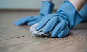 Mani con guanti blu puliscono un pavimento in legno con un panno, creando un detersivo pavimenti fai da te.