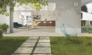 Modern patio with stone pavers, grass, and outdoor seating, opening to a bright, open-plan living and kitchen area.