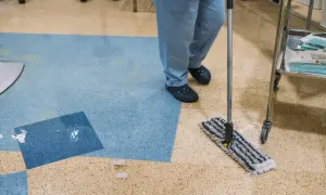 Persona con camice blu lava linoleum con alcool, usando uno straccio.
