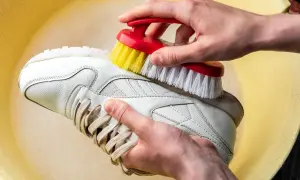 Mani che lavano scarpe di tela bianche a mano con una spazzola in una bacinella gialla.