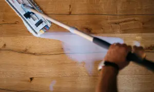 Mano che pulisce un pavimento in legno non trattato con uno straccio umido.