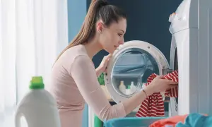 Donna carica la lavatrice, pensando a come la varechina cos'è e a come usarla per sbiancare i capi.